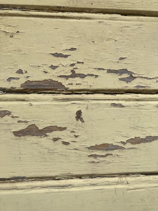 Gulnad fasad med avskavd färg och blottat trä, visar pågående skrapningsarbete inför renovering.