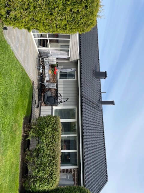 Bild på ett hus med nyligen målat svart tak, omgiven av grön gräsmatta och trädgårdsmöbler på altanen.