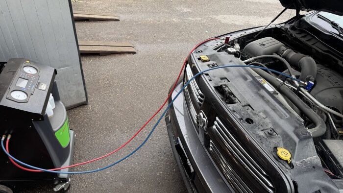 Bilen fylls med köldmedium via en maskin med två slangar, en röd och en blå, anslutna till bilens öppen motorhuv.