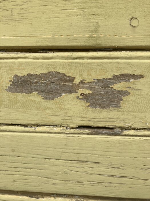 En närbild av en trävägg med gul färg som har skrapats bort på vissa ställen, vilket exponerar träet under.