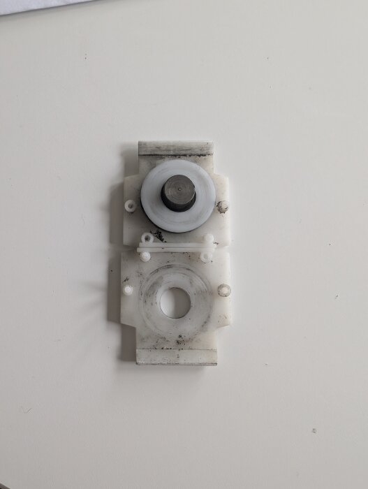 Hjulvagga med ett skjutdörrshjul som är delvis skadat och slitet, placerad på en vit yta.