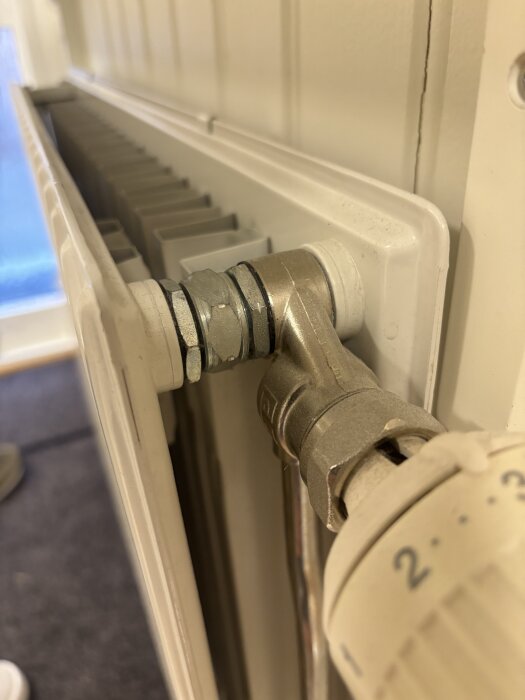 Radiator kopplad till vägg med metallfästen, synlig termostatventil och insexskruv.