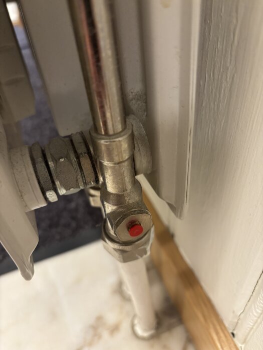 Radiatorkoppling med insexskruv och röd plastknopp, ansluten till ett rör, närbild.