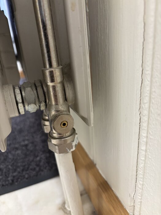 Radiatorkoppel med synlig röranslutning mot väggen, ovanför finns en avstängningsventil delvis skyddad av en röd plastknopp.
