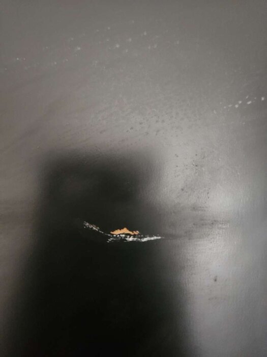 Svartlackerad säkerhetsdörr med tydliga repor och avflagad färg i mitten.