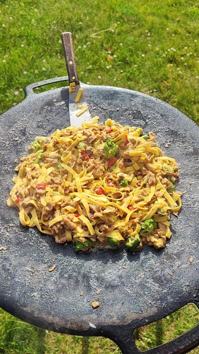 En murikka med pasta, köttfärs, broccoli och paprika lagad utomhus på ett gräsmatta.