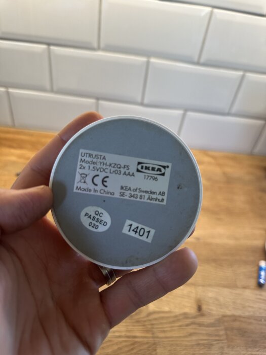 En person håller en rund fjärrkontroll med etikett "Utrusta Model YH-KZQ-FS" från IKEA i köksmiljö.