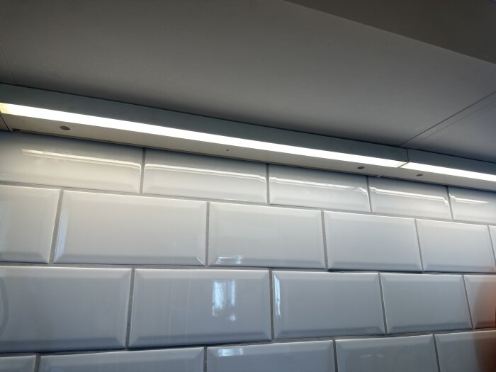 LED-belysning under köksskåp med vita kakelplattor i bakgrunden, en av tre lampor tänd efter strömavbrott.