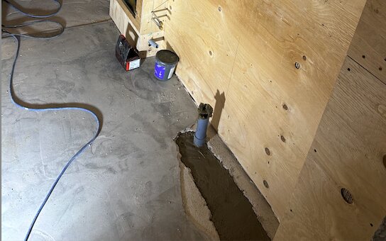 Flyttat avloppsrör under handfat och gjutning av höjd botten i badrum, syns bredvid en träpanel och diverse byggmaterial.