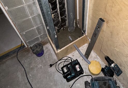 Verktyg och material vid flytt av rör, där avloppsrör har flyttats under handfatet. Sladdar, en borrmaskin och andra verktyg syns på golvet.