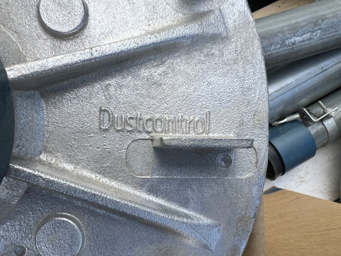 Närbild på en metalldel märkt "Dustcontrol", omgiven av rör och kopplingar, relaterat till en spånsuganläggning för ett snickeri.