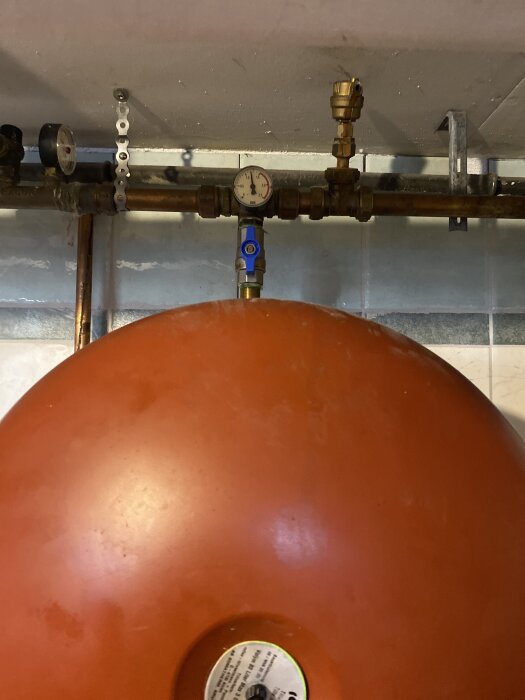 En röd expansionskärl med tryckmätare och rörkopplingar synliga under installation av ny kran, varmvattenproblem nämns i texten.