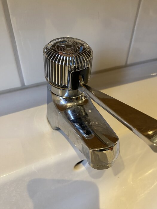 Kran av modell Mora från ca 2006, med en silverfärgad spak och en räfflad plasttopp som användaren försöker demontera för smörjning.