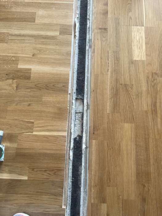 En smal lång skåra i ett trägolv, där en vägg tidigare stod, behöver fyllas igen för att matcha golvets nivå.