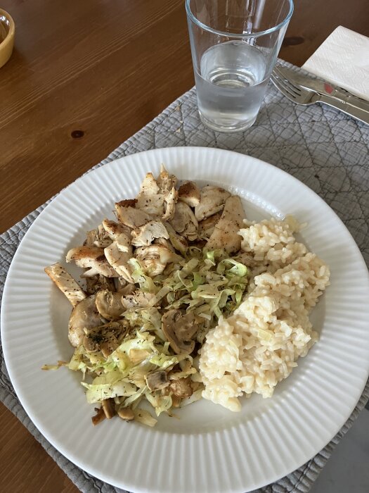 Tallrik med risotto, spetskål, champinjoner och grillad kyckling. Glas vatten bredvid.