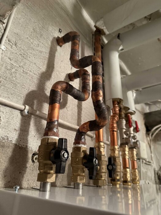 Kopparrör i kringelikrog-mönster anslutna till en fjärrvärmecentral, visar komplex rördragning och ventiler.