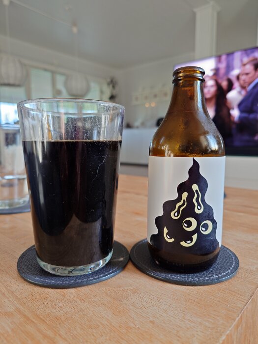 Ett glas och en flaska stout på ett bord, etiketten prydd med ett konstnärligt motiv.
