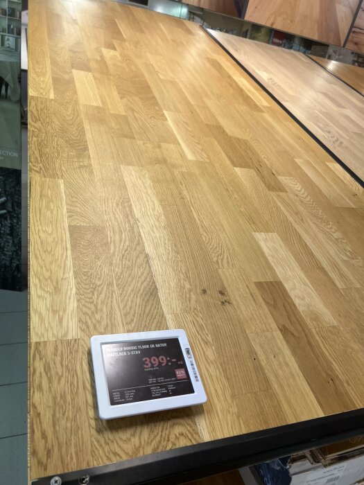 Ekparkettgolv på visningsyta med prisetikett, "Trägolv Nordic Floor Ek Natur, Mattlack 3-stav, 399 kr/m2," i butiksmiljö.