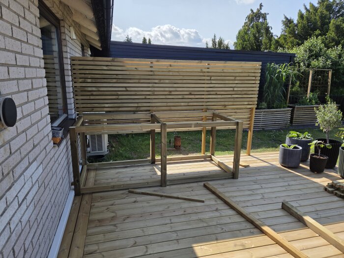Trädäck med trästomme för utekök under konstruktion, med plankor och ytor för grill och växter i krukor vid sidan.