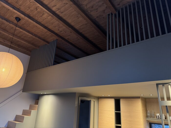 Loft med träpaneler i taket, moderna träräcken och en stor rund lampa.