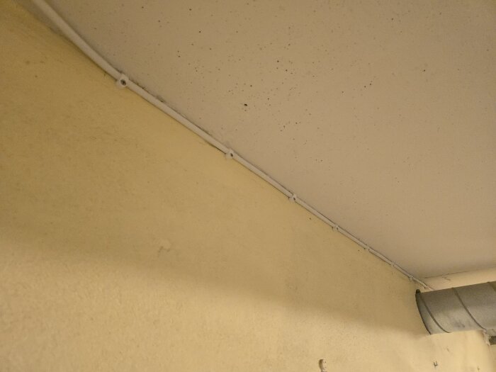 Kabel monterad längs ett gult innertak, med ett ventilationsrör i hörnet, under pågående renovering i förråd.