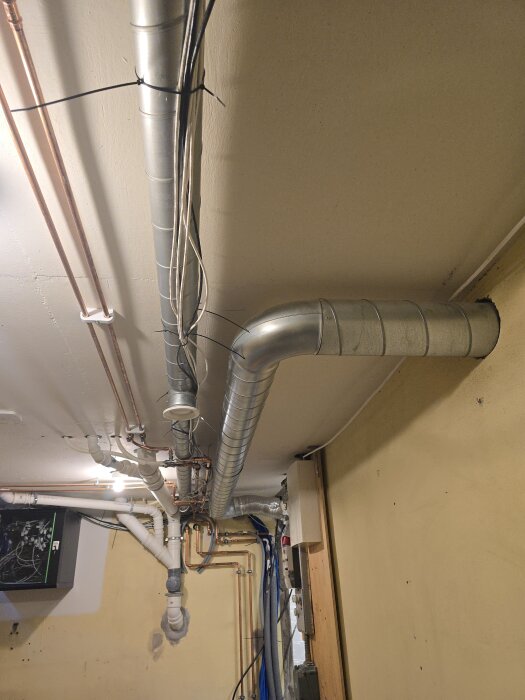 Tak av ett rum med flera metalliska ventilationsrör och kablar monterade.