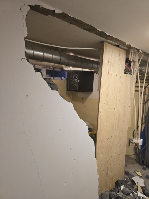 En delvis riven vägg med synliga rör och elinstallationer, omgiven av nerfallet material i ett förråd under renovering.