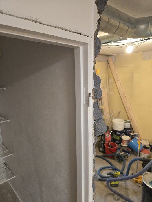 En delvis riven vägg, synliga ventilationsrör, målarburkar, verktyg och en del stök i ett renoveringsområde.