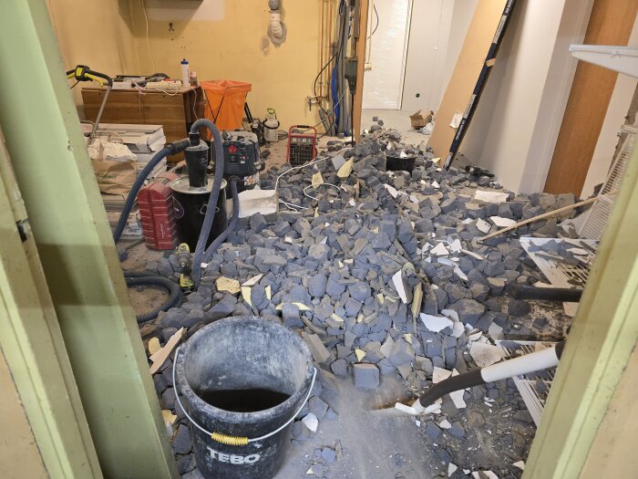 Renoveringsprojekt: ett förråd fullt av rivningsmaterial och verktyg under pågående väggborttagning. Golvet täckt av betongbitar och byggavfall.