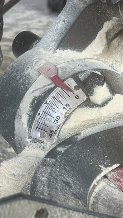 Gradering på en kap- och gersåg, visar vinklar från 0 till 45 grader åt båda håll, med damm och sågspån runt mätaren.