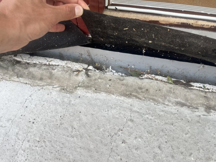 Håller upp bortvikt papp eller filt framför en spricka i betong nära en dörrkarm där isoleringen är synlig.