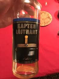 Flaska med etiketten "Kapten Löjtnant Likör" på ett rödaktigt underlag.