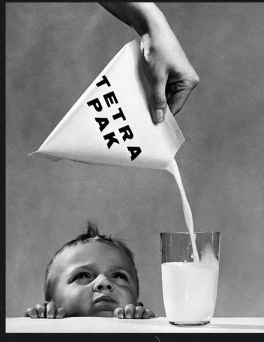 En hand håller en Tetra Pak-förpackning och häller mjölk i ett glas bredvid ett barns ansikte på ett svartvitt foto.