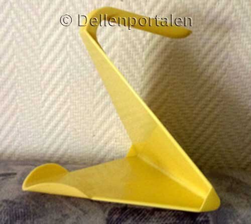 Gul hållare för att hälla tetra-förpackningar, formad som en Z, placerad mot en vägg.