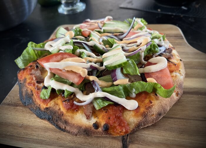 Kebabpizza toppad med sallad, tomat och dressing på en bakplåt.