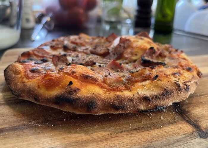 Hembakad kebabpizza med grönsaker och kebabsås på en träskärbräda, närbild på krispig kant.