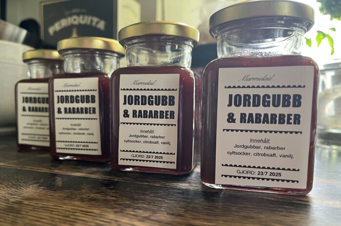 Fyra burkar jordgubb- och rabarbermarmelad med etikettfel, på ett träbord.