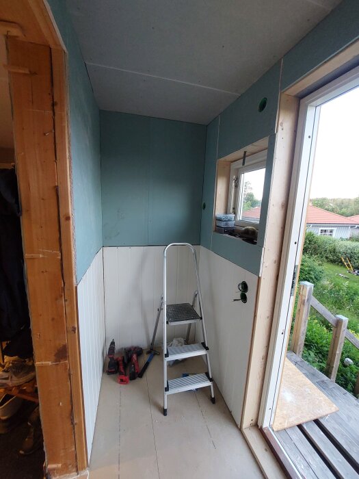 Invändig byggprojekt med gips och panel färdig, stege och verktyg syns i rummet med öppet fönster och skev perspektiv.