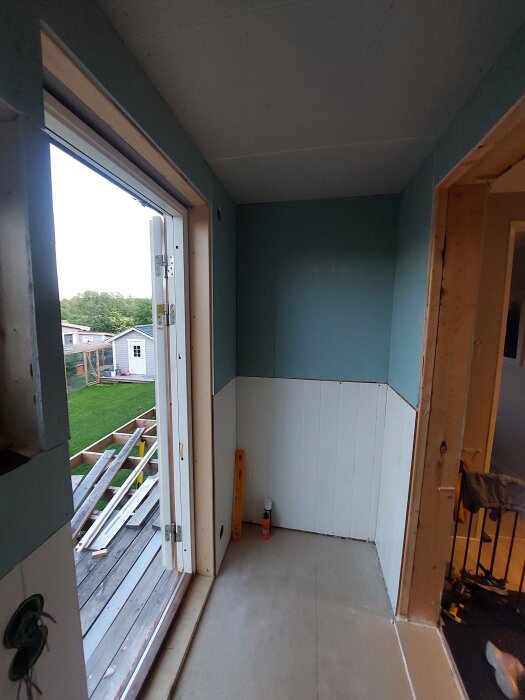Invändig renovering med klar panel och gipsväggar, visar ett rum med utgång till altan och träreglar utanför. Perspektivet är skevt.