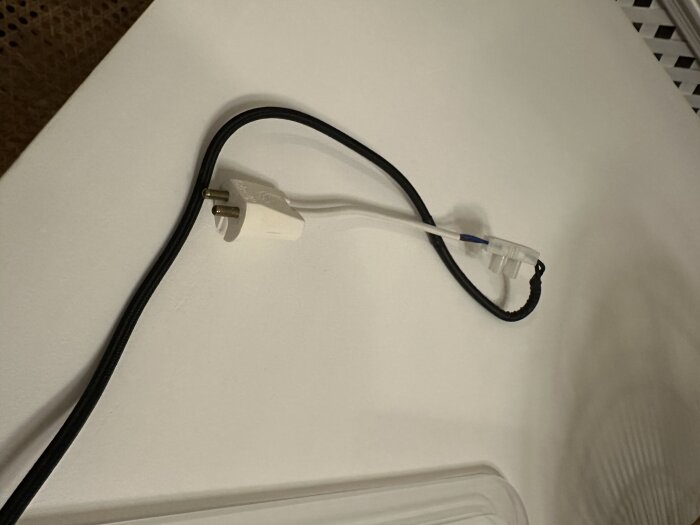 Svart och vit elkabel ansluten till en lamppropp via en sockerbit på ett vitt tak.