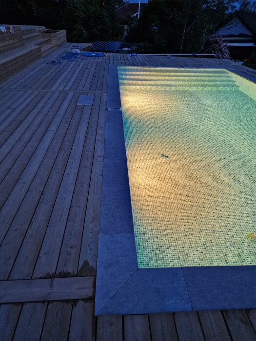 Stensarg runt en pool i skymning, med bruna trädäckplankor runtomkring. Stenarna går inte jämnt upp och olika alternativ för att justera diskuteras.