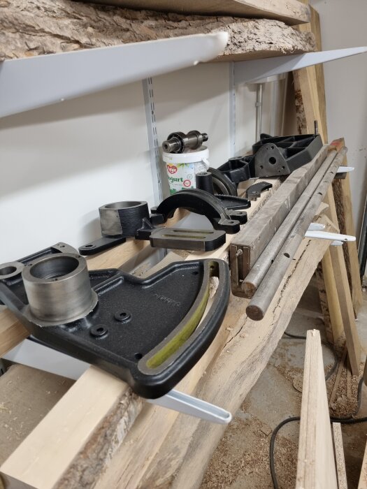 Metalldelar och verktyg på en hylla, bland träbitar; ett renoveringsprojekt med fokus på spackling och grundning av sågskåp av gjutjärn.