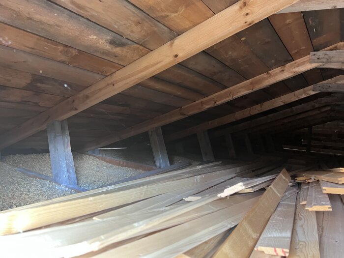 Loftutrymme med synliga takstolar och träpanel, där takhöjden är låg och byggmaterial ligger på golvet.
