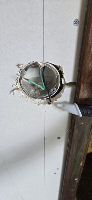 Vägguttag med synliga gröna och svarta elkablar, samt en spänningsprovare under användning.