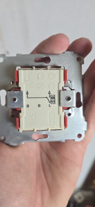 Strömbrytare med kopplingsschema "L", "B", och pilar, hålls i en hand, märkt "S16" och "Elko".