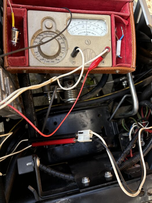 Multimeter ansluten till elkablar i fordon, används för felsökning vid batterireparation.