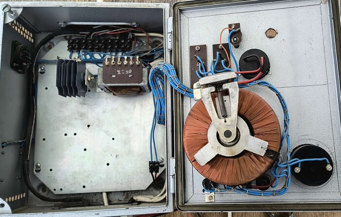 En gammal elektrisk apparat med blå ledningar och en stor kopparlindad komponent i ett metallhölje, sannolikt från 1950-talet.