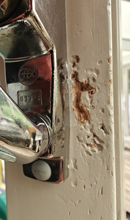 Skadad dörrkarm vid dörrhandtag med avskavd färg och träexponering, lämpad för reparation med spackel eller kemiskt trä.