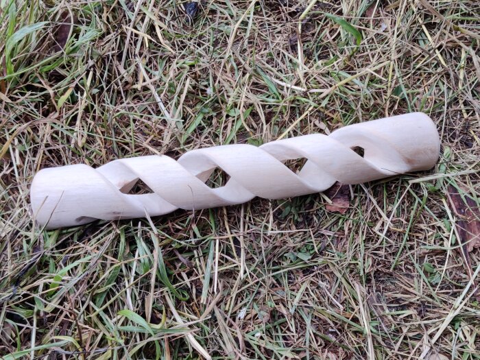 Träskruv eller lägerstift med spiralformad design liggande på gräs.