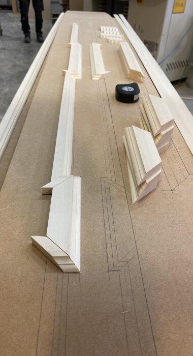 Träbitar i olika storlekar och former ligger utlagda på en skiva, som en del av ett dekorprojekt för att täcka dörrmaskiner i en samlingslokal.